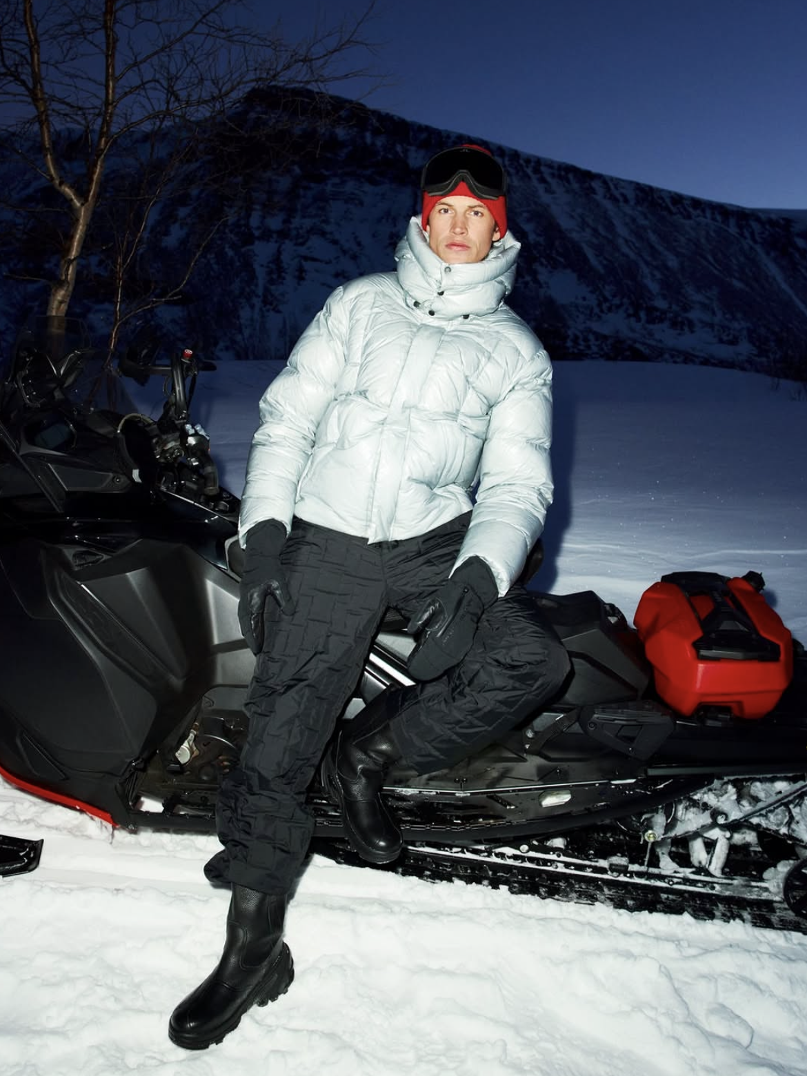 Model in a metallic-white down puffer jacket beside a snowmobile at night